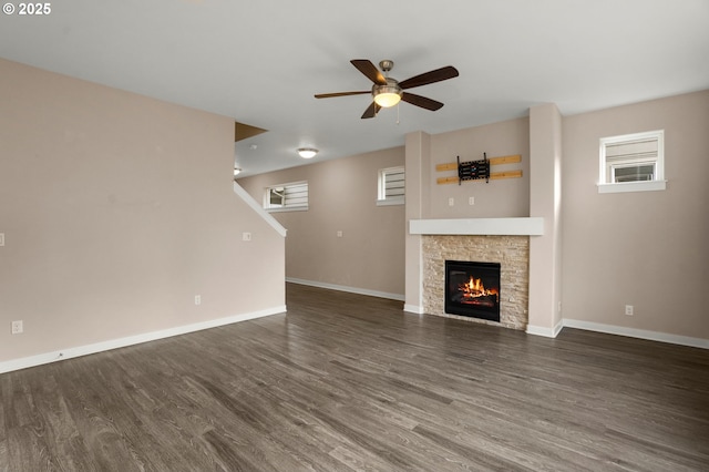 unfurnished living room featuring ceiling fan, baseboards, wood finished floors, and a stone fireplace