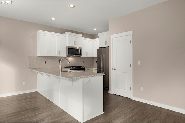 kitchen featuring a peninsula, white cabinetry, appliances with stainless steel finishes, backsplash, and dark wood finished floors