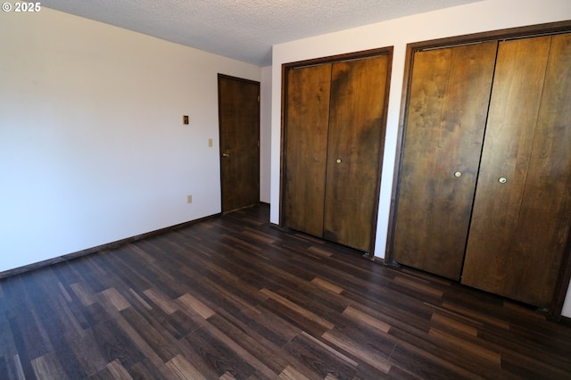 unfurnished bedroom featuring a textured ceiling, two closets, and dark hardwood / wood-style flooring