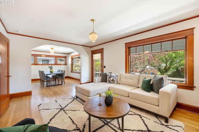 living room featuring arched walkways, crown molding, light wood finished floors, and baseboards