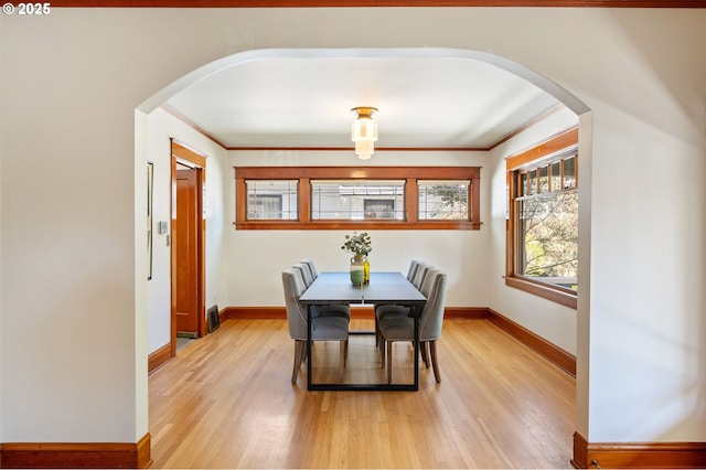dining space with arched walkways, baseboards, and light wood-style floors