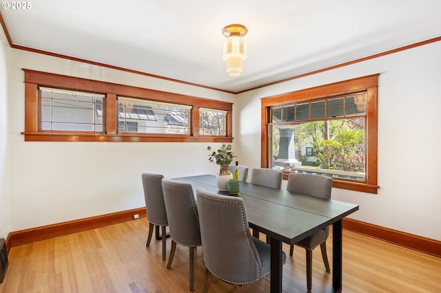 dining room with light wood-type flooring, crown molding, and baseboards