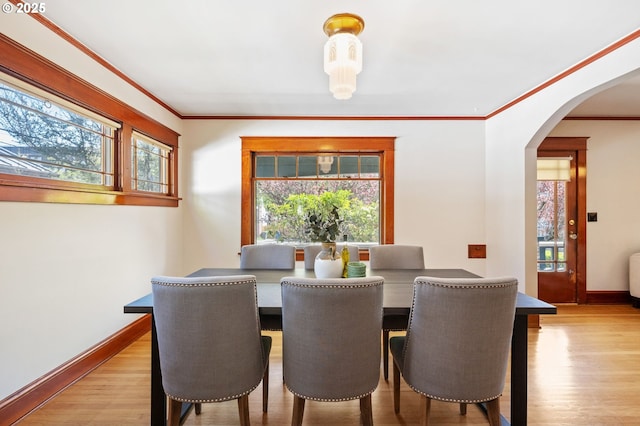dining area featuring arched walkways, wood finished floors, baseboards, and ornamental molding