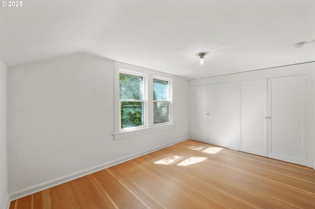 unfurnished bedroom with light wood-style flooring, multiple closets, lofted ceiling, and baseboards