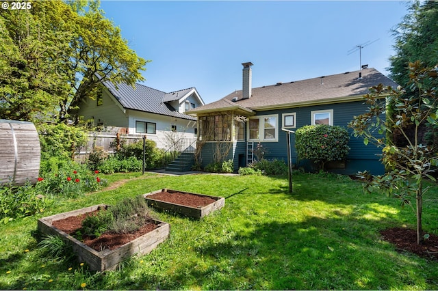 back of property featuring a garden, a chimney, fence, and a lawn