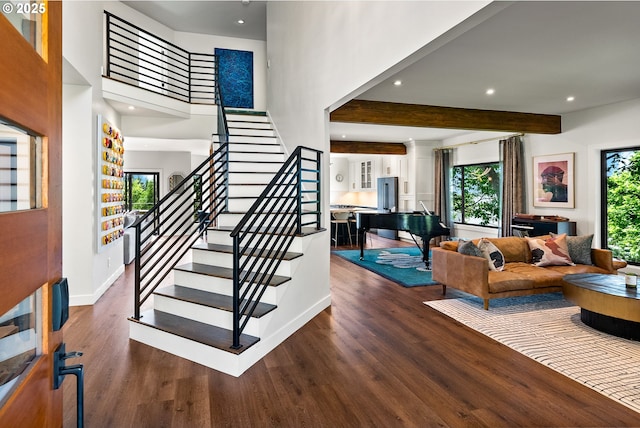 staircase with a towering ceiling, wood finished floors, beamed ceiling, baseboards, and recessed lighting