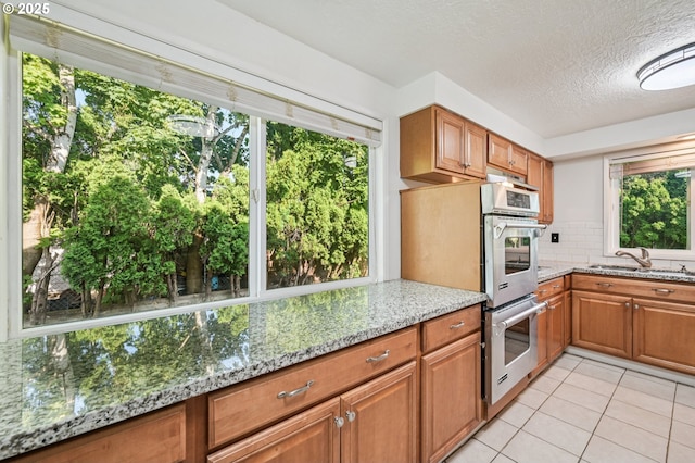 1631 N Clark St, Cornelius, OR 97113 - kitchen with double oven, light tile patterned floors, brown cabinets, light stone counters, and a textured ceiling