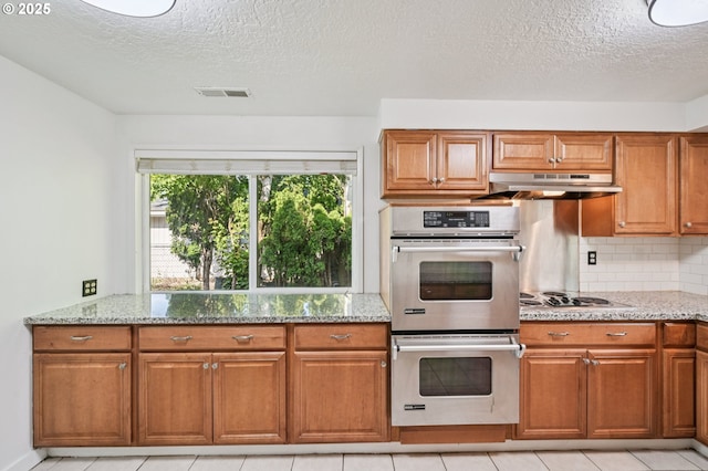 1631 N Clark St, Cornelius, OR 97113 - kitchen with stainless steel double oven, under cabinet range hood, brown cabinetry, light stone countertops, and decorative backsplash