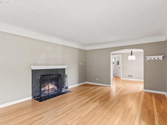 4561 NE 35th Ave, Portland, OR 97211 - unfurnished living room with a premium fireplace, a textured ceiling, light wood-style floors, arched walkways, and crown molding