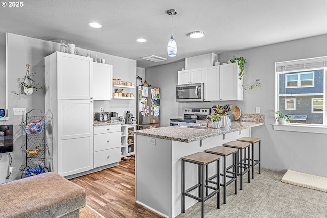 kitchen featuring kitchen peninsula, pendant lighting, a breakfast bar area, white cabinets, and appliances with stainless steel finishes