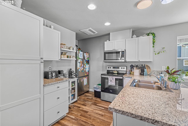 kitchen with a textured ceiling, stainless steel appliances, sink, wood-type flooring, and white cabinets