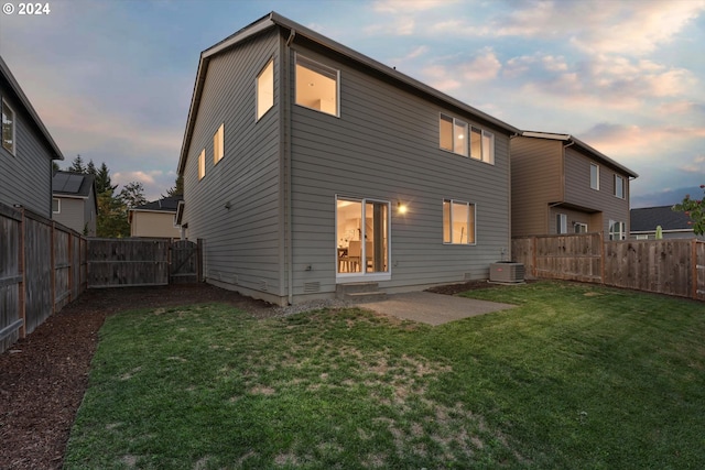 back of house at dusk with a gate, a patio, central AC, a fenced backyard, and a yard