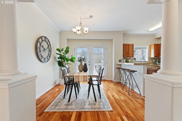 dining room featuring an inviting chandelier, decorative columns, light wood finished floors, and ornamental molding