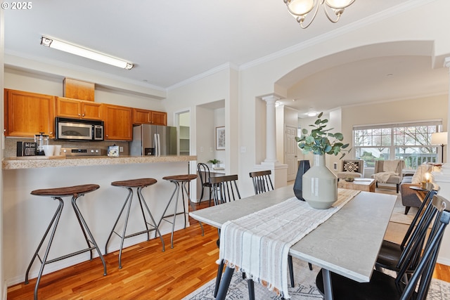 dining room with light wood finished floors, arched walkways, ornate columns, and ornamental molding