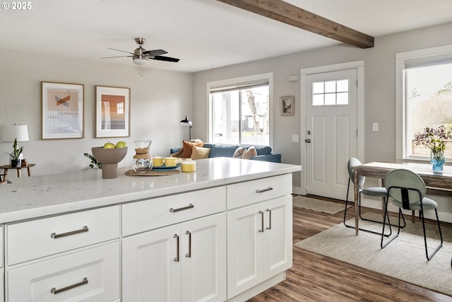 kitchen featuring ceiling fan, light stone countertops, white cabinets, dark hardwood / wood-style flooring, and beamed ceiling