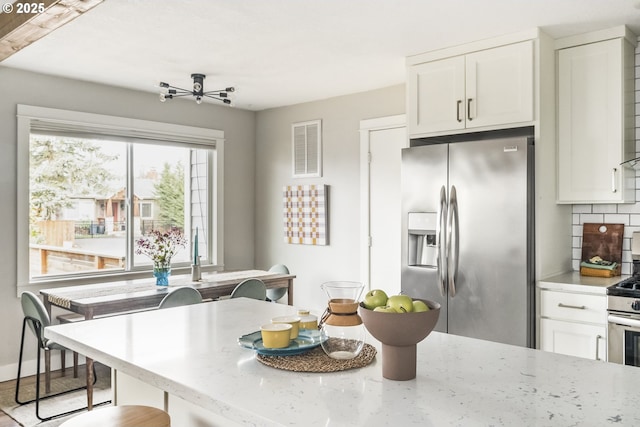 kitchen featuring backsplash, stainless steel appliances, light stone countertops, white cabinets, and a kitchen bar