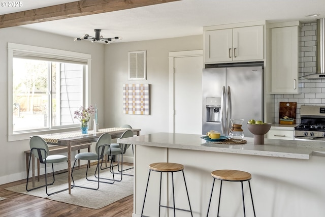 kitchen with wall chimney range hood, light hardwood / wood-style flooring, appliances with stainless steel finishes, white cabinetry, and backsplash