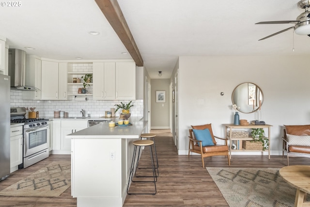 kitchen featuring stainless steel appliances, a kitchen breakfast bar, wall chimney exhaust hood, white cabinets, and beamed ceiling