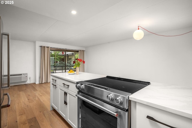 1919 NW Hoyt St Unit 104, Portland, OR 97209 - kitchen featuring stainless steel range with electric stovetop, white cabinetry, light wood-style floors, an AC wall unit, and recessed lighting