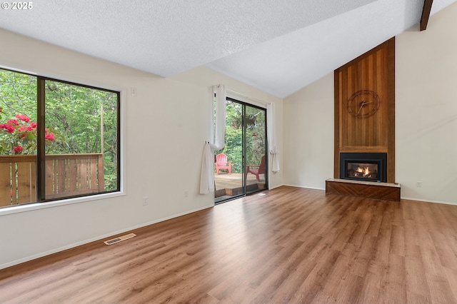 unfurnished living room featuring vaulted ceiling, a large fireplace, wood finished floors, and visible vents