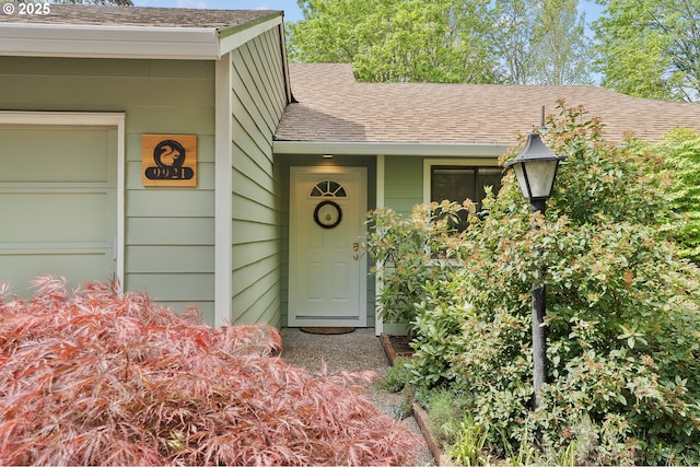 view of exterior entry with a shingled roof and an attached garage