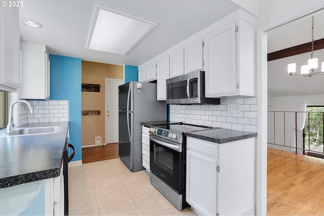 kitchen featuring stainless steel appliances, a notable chandelier, white cabinetry, and a sink