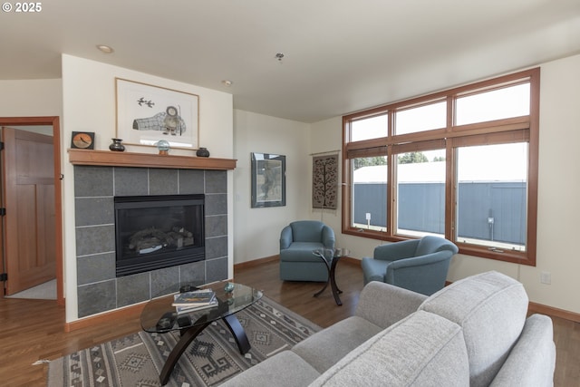 living room featuring a tile fireplace, baseboards, and wood finished floors