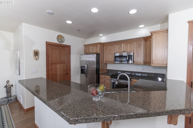 kitchen featuring recessed lighting, dark stone counters, appliances with stainless steel finishes, a peninsula, and dark wood-style flooring