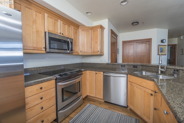 kitchen featuring light brown cabinets, a sink, wood finished floors, stainless steel appliances, and dark stone counters