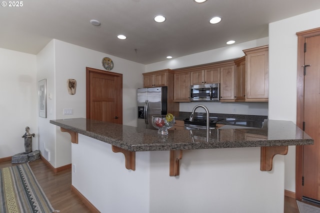 kitchen featuring a breakfast bar, a peninsula, recessed lighting, stainless steel appliances, and dark wood-type flooring