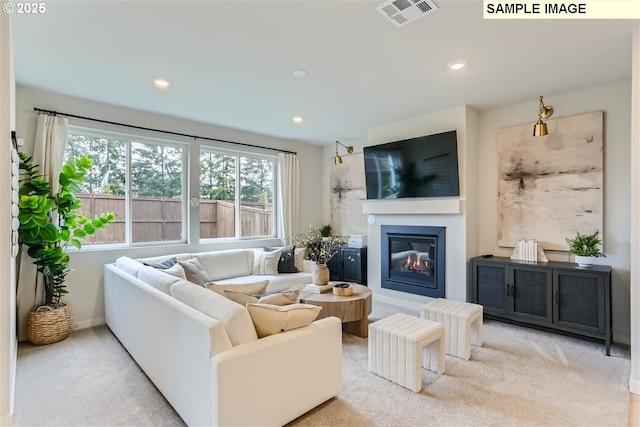 carpeted living area featuring recessed lighting, visible vents, baseboards, and a glass covered fireplace