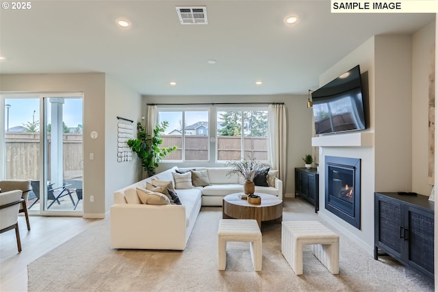 living room with a glass covered fireplace, visible vents, plenty of natural light, and recessed lighting