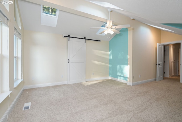 unfurnished room featuring light colored carpet, lofted ceiling with skylight, a barn door, and ceiling fan