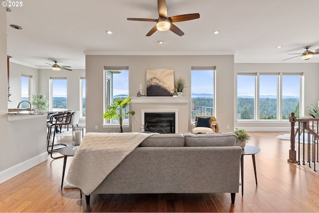 living room with wood finished floors, baseboards, recessed lighting, a glass covered fireplace, and crown molding