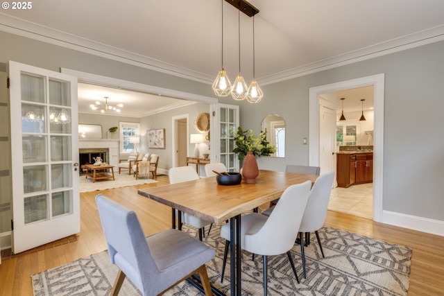 dining area featuring crown molding, a fireplace, arched walkways, and light wood finished floors