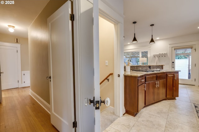 interior space featuring stainless steel gas stovetop, brown cabinetry, light tile patterned floors, light stone countertops, and hanging light fixtures