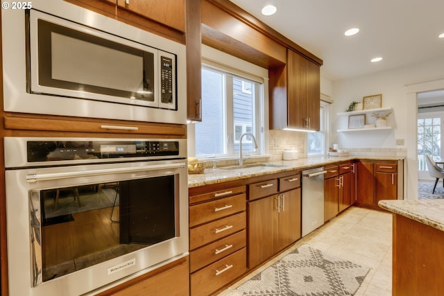 kitchen with tasteful backsplash, a sink, light stone counters, appliances with stainless steel finishes, and open shelves