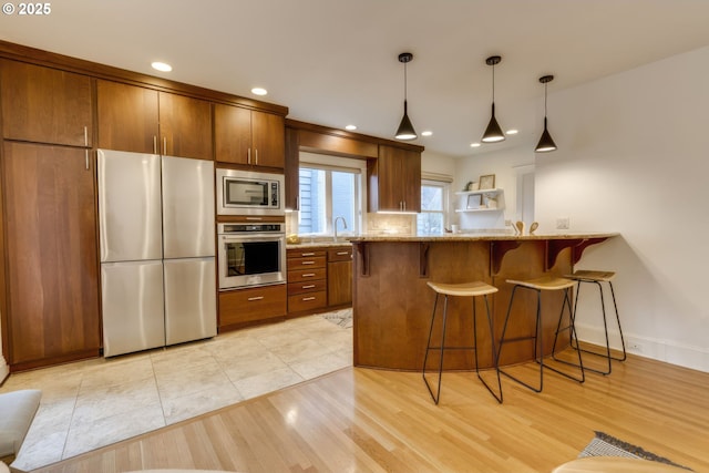 kitchen featuring light stone countertops, a kitchen bar, light wood-style flooring, hanging light fixtures, and stainless steel appliances