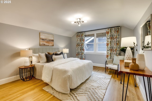 bedroom with light wood-type flooring, baseboards, and vaulted ceiling