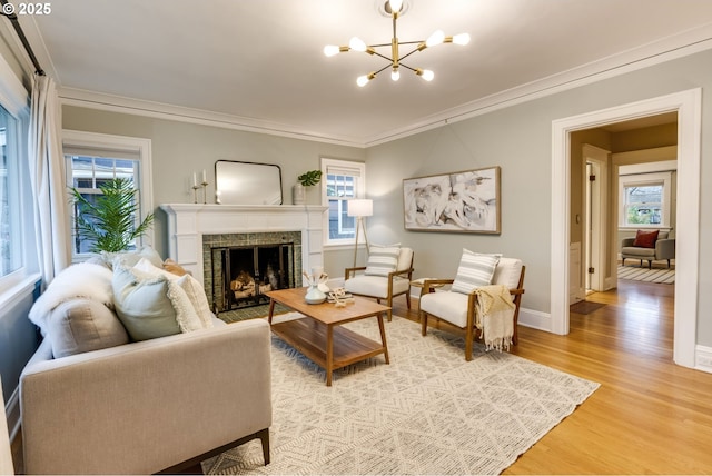 living area with baseboards, light wood-type flooring, ornamental molding, a fireplace, and an inviting chandelier