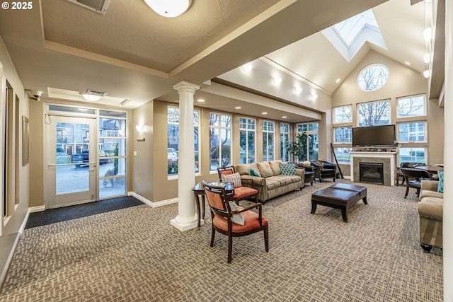 carpeted living room featuring a towering ceiling, a tiled fireplace, and decorative columns