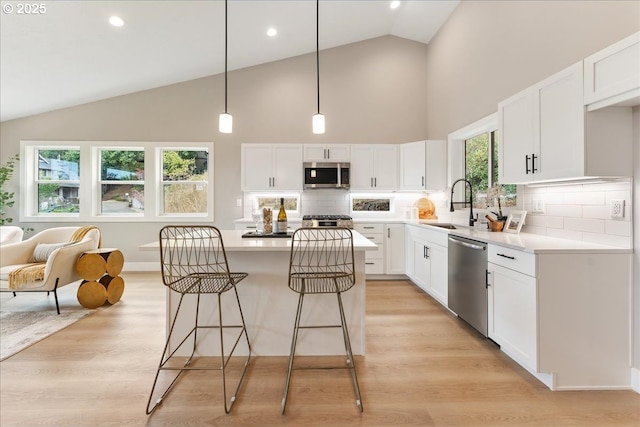 kitchen with a kitchen island, appliances with stainless steel finishes, decorative light fixtures, white cabinetry, and sink