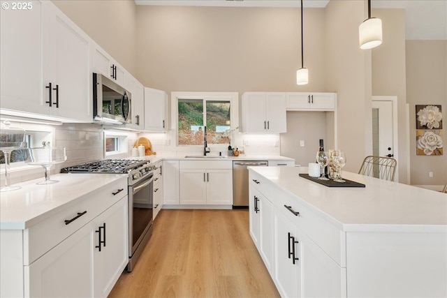 kitchen featuring white cabinetry, stainless steel appliances, sink, and hanging light fixtures