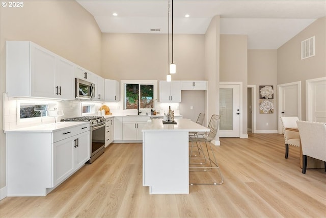 kitchen with a towering ceiling, white cabinetry, hanging light fixtures, a center island, and stainless steel appliances