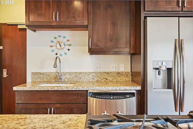 kitchen featuring dark brown cabinets, appliances with stainless steel finishes, light stone counters, and a sink