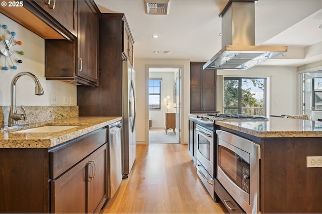 kitchen with visible vents, island range hood, stainless steel appliances, dark brown cabinets, and a sink