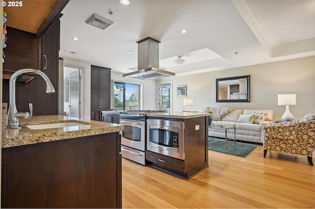 kitchen with light wood-style flooring, island exhaust hood, appliances with stainless steel finishes, and a sink