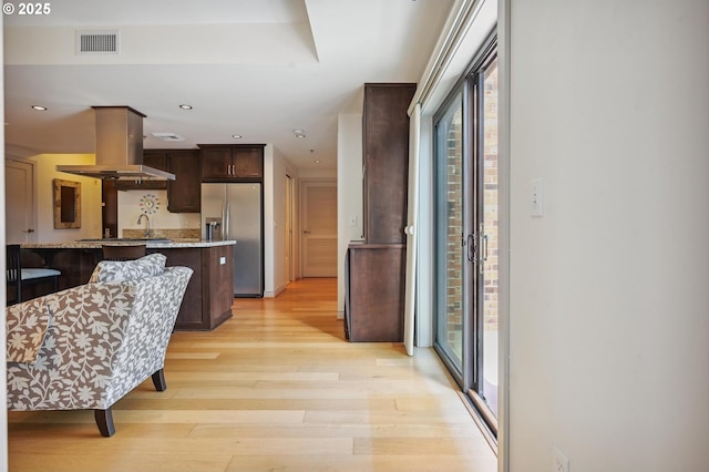 kitchen with island exhaust hood, stainless steel refrigerator with ice dispenser, visible vents, light wood-style floors, and dark brown cabinets