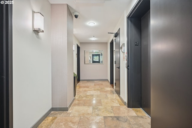 hall with stone tile flooring and baseboards