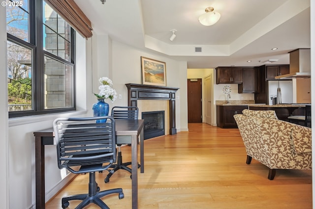 dining space featuring light wood-type flooring, visible vents, a fireplace, and a tray ceiling